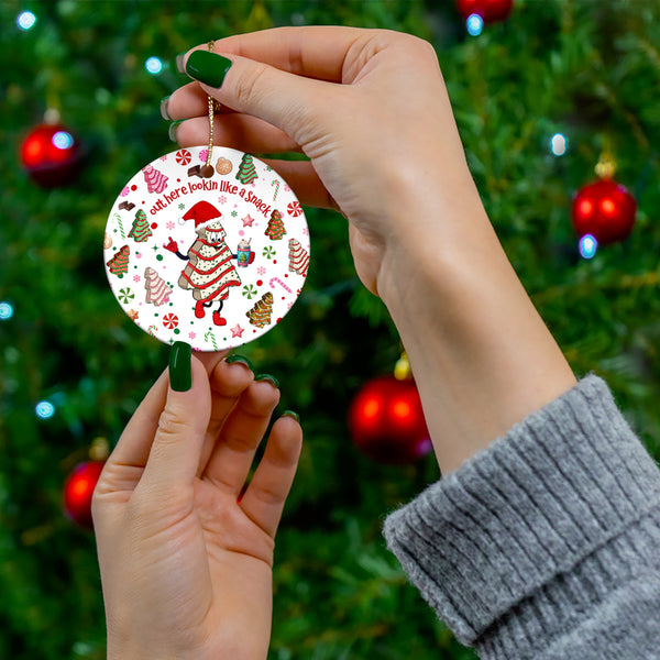 Holiday-themed Print-On-Demand ornament featuring a whimsical gingerbread-inspired figure wearing a Santa hat, surrounded by festive elements like candy canes, Christmas trees, and cookies. The text reads ‘Out Here Lookin’ Like a Snack’ in a playful font. Perfect for adding a touch of humor and charm to your holiday decorations.