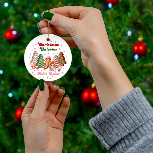 Round ceramic ornament featuring a festive design of Christmas trees, a gingerbread character, and the phrase ‘Christmas Calories Don’t Count.’ Perfect for holiday décor or gifting.