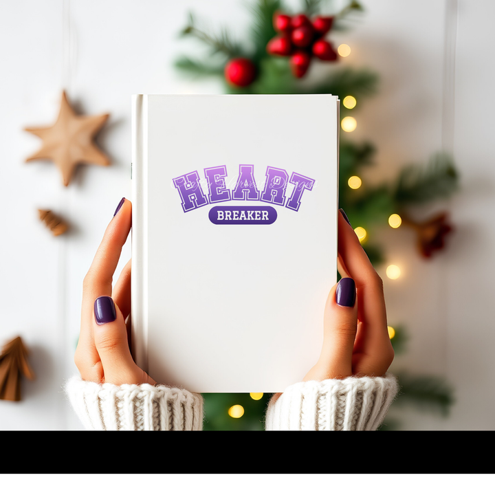 Hands holding a white notebook featuring the ‘Heartbreaker’ design in purple varsity-style text.