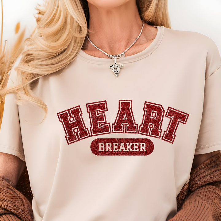 a model wearing a beige t-shirt featuring the ‘Heartbreaker’ design in bold red glitter varsity-style text.