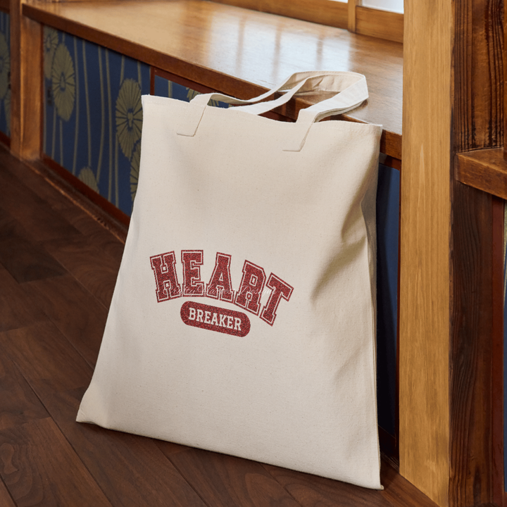 Beige tote bag featuring the ‘Heartbreaker’ design in bold red glitter varsity-style text