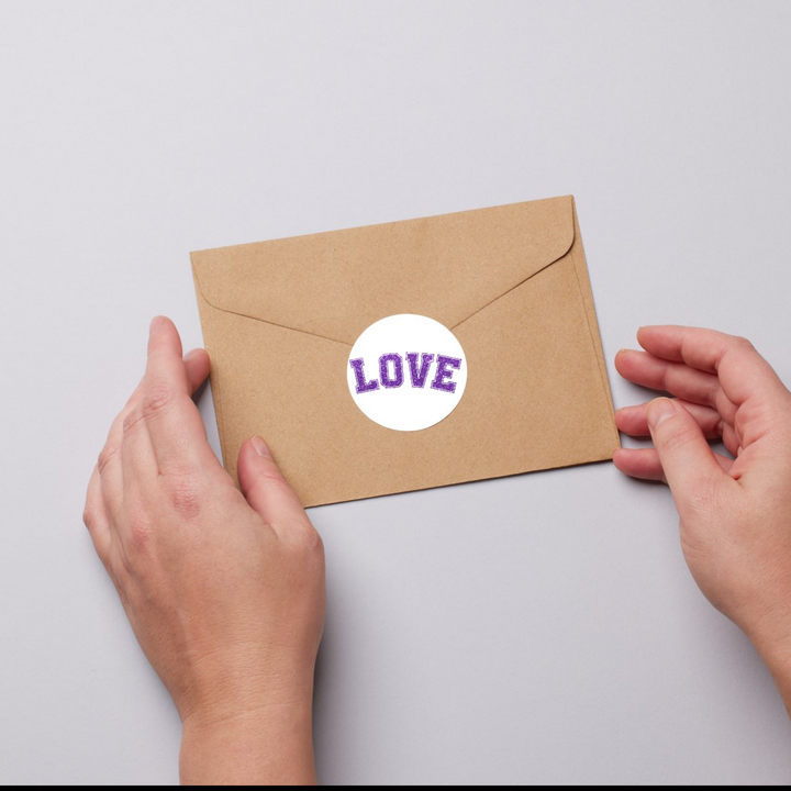 Kraft envelope sealed with a circular sticker featuring the ‘Love’ design in purple varsity-style text.