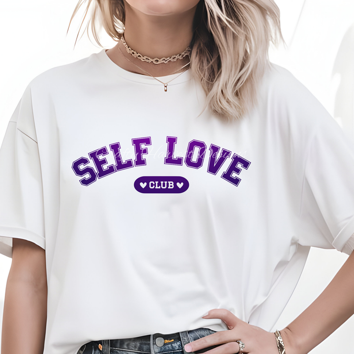 Model wearing a white t-shirt featuring the ‘Self Love Club’ design in purple varsity-style text with heart accents.