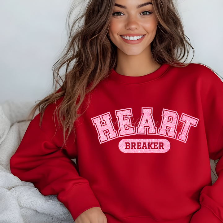 Red sweatshirt featuring the ‘Heartbreaker’ design in pink glitter varsity-style text.